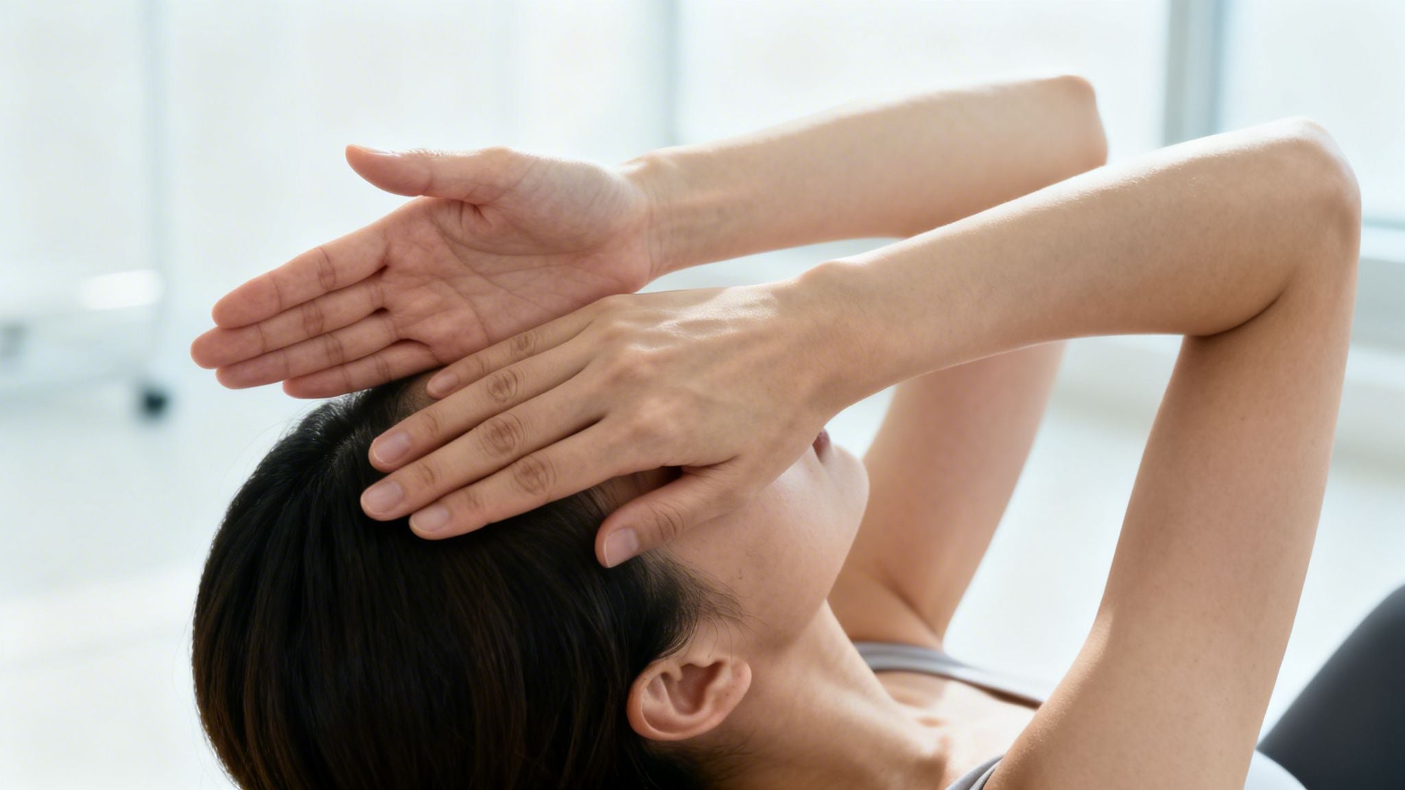 A woman lies down, hands covering her forehead, possibly stretching or relaxing.