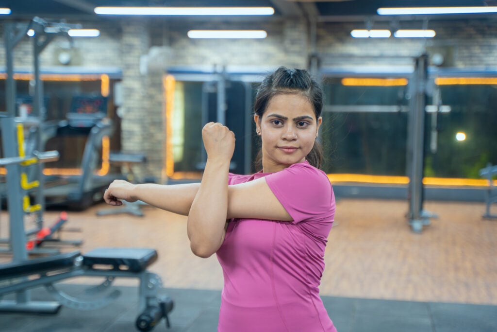 Woman Performing Cross Body Shoulder Stretch Exercise During Workout in Gym