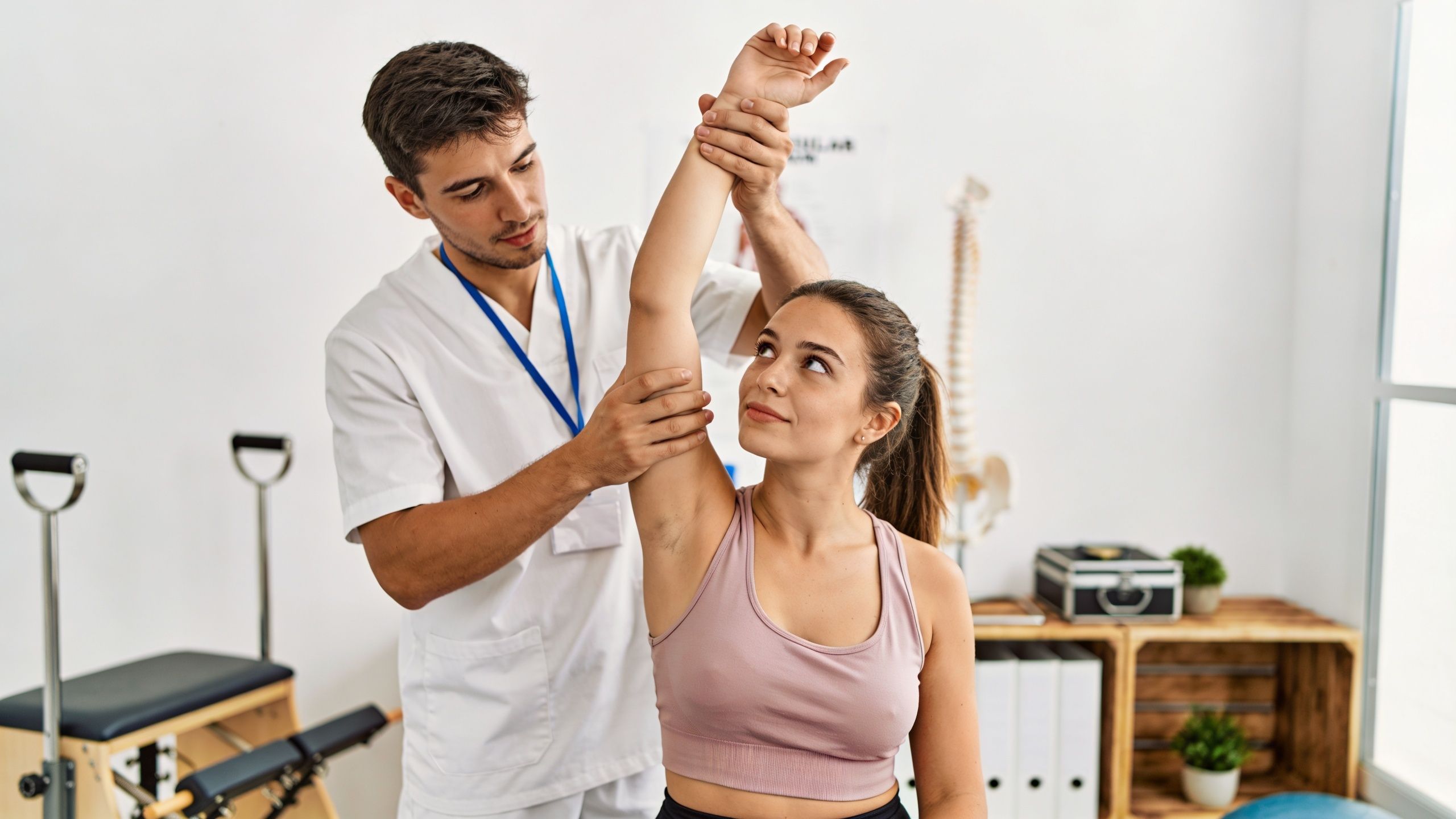 A professional male physical therapist stretching the arm and shoulder of a young woman in a clinic.