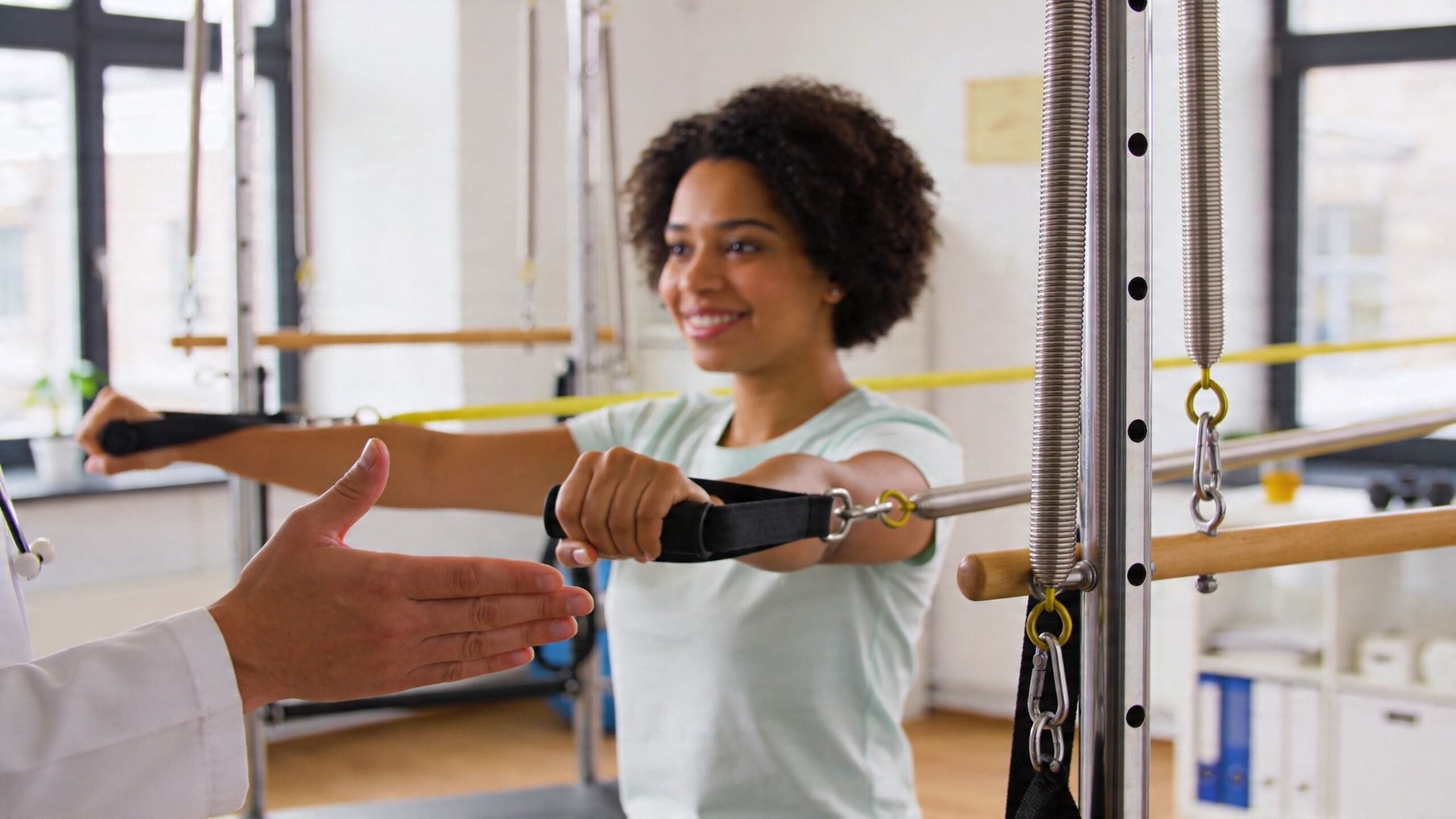 A physical therapist guides a patient performing resistance exercises on a pilates machine in a bright clinic.